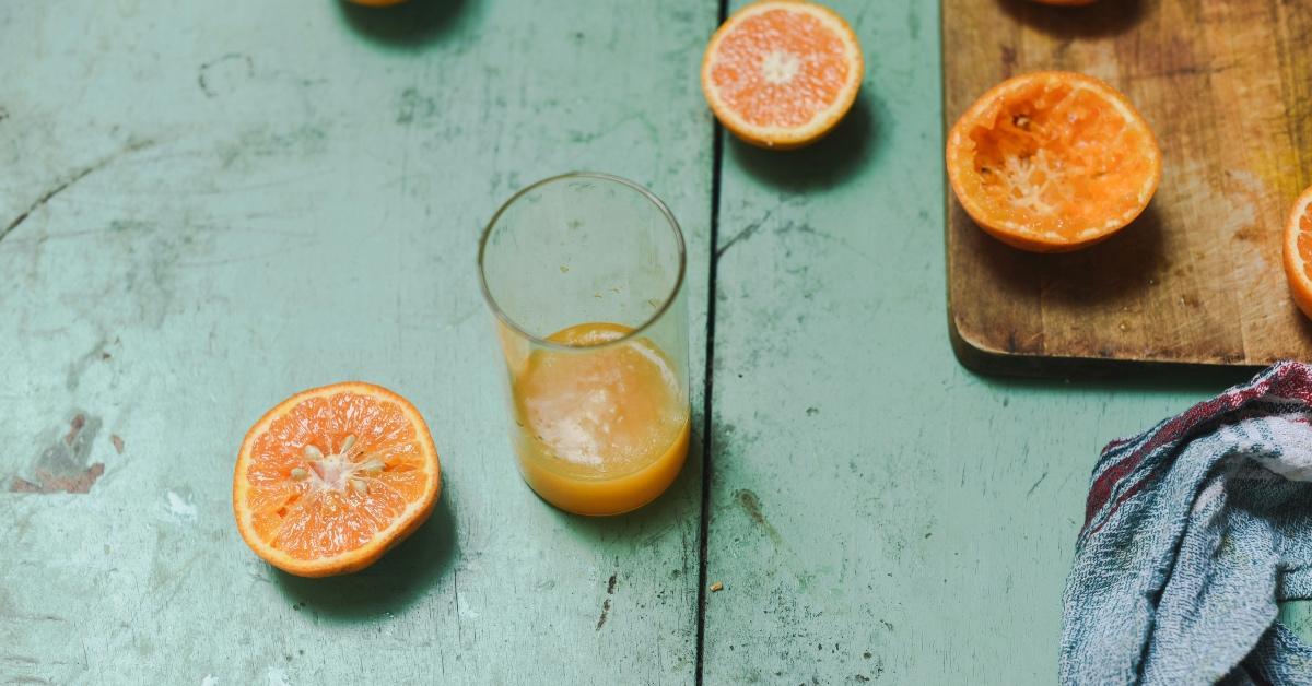 Glass of freshly-squeezed orange juice on a blue table with oranges. 