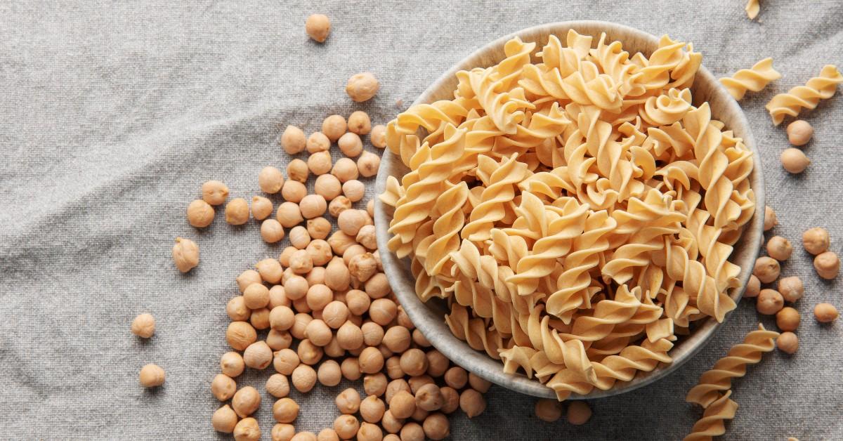 A bowl of chickpea pasta sits nestled amongst loose chickpeas on a cloth backdrop