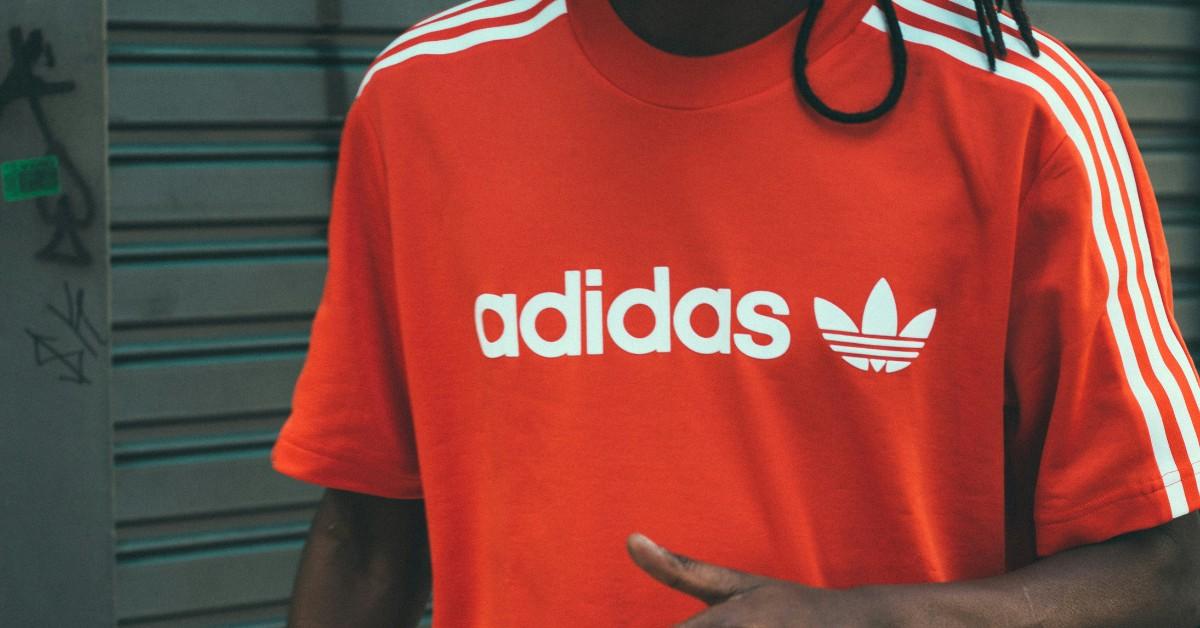 A man wears a red shirt with the Adidas logo across the front in white