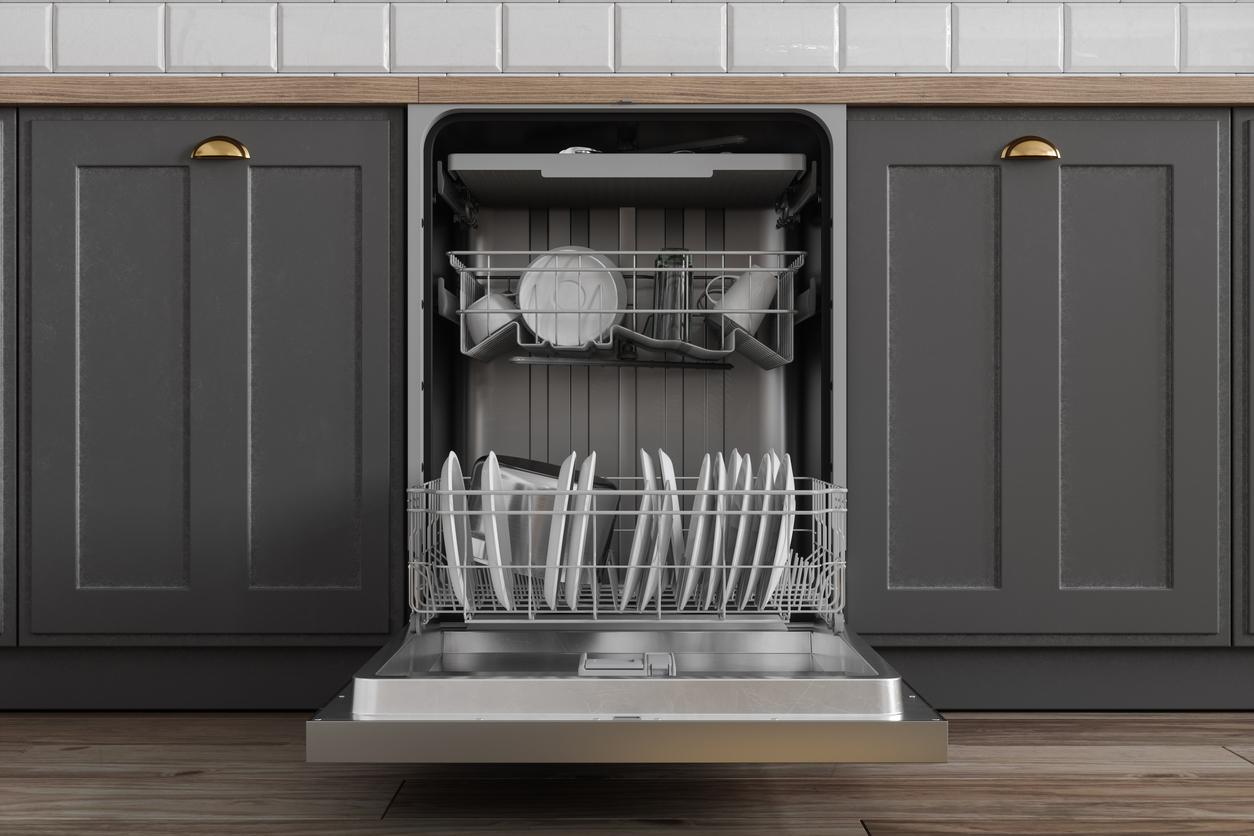 A dishwasher is pictured tucked into a gray and gold cabinet with dishes neatly spaced apart.