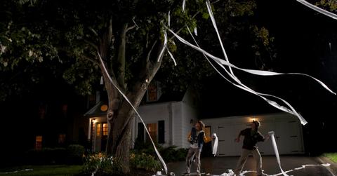 Two boys throwing toilet paper into a tree in front of a house at night.