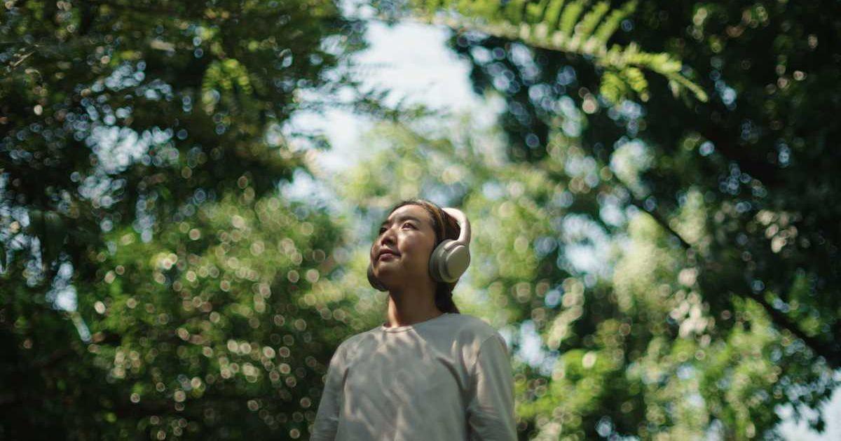 A woman wears headphones while relaxing in nature (Representative Cover Image Source: Getty Images | pocketlight)