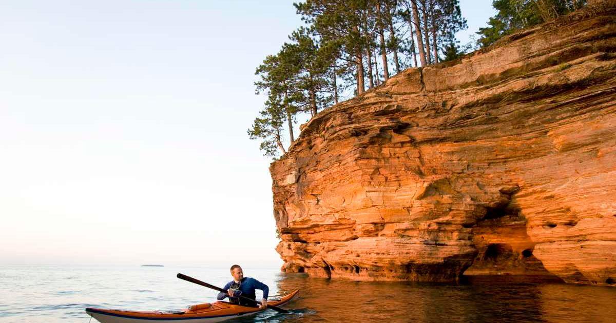 Person kayaking near a red sandstone rocky structure in Sand Island, Apostle Islands in Wisconsin (Representative Cover Image Source: Getty Images | JMichi)