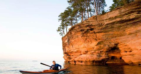 Person kayaking near a red sandstone rocky structure in Sand Island, Apostle Islands in Wisconsin (Representative Cover Image Source: Getty Images | JMichi)