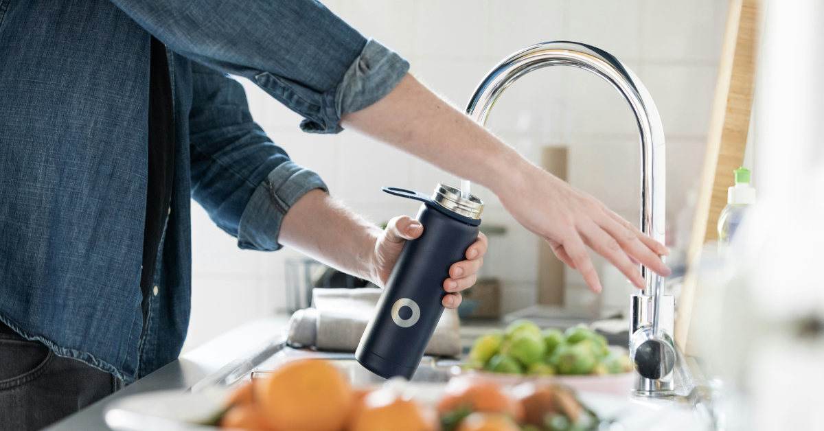 A person fills a water bottle from their kitchen sink