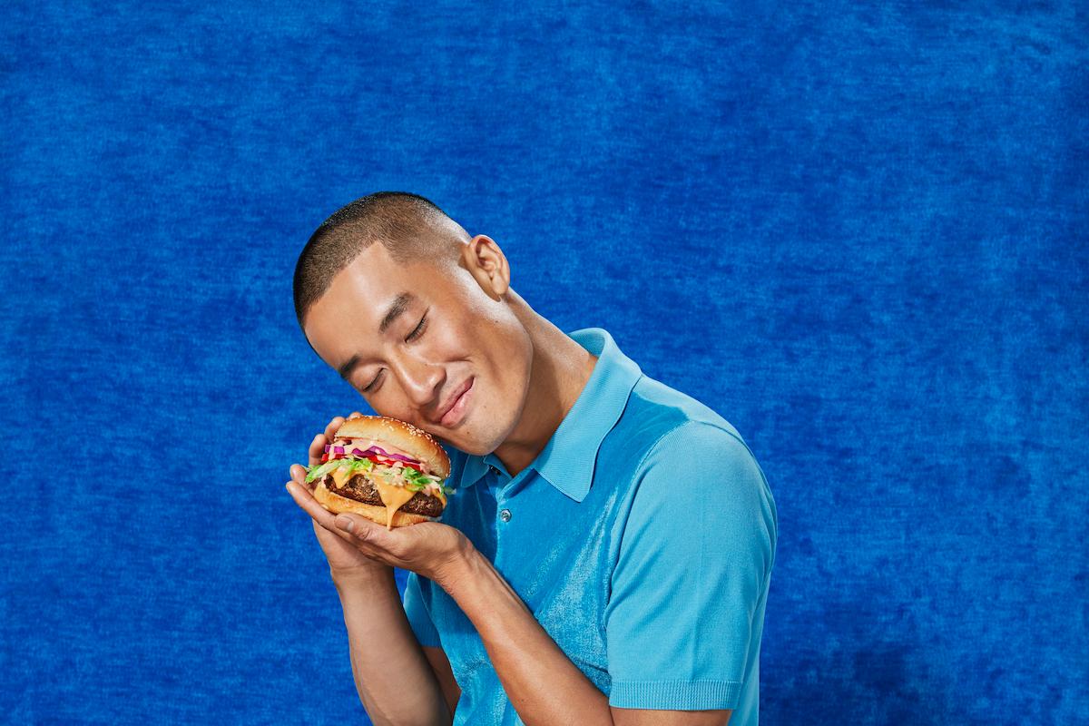 Man holds an Impossible Burger up to his cheek. 