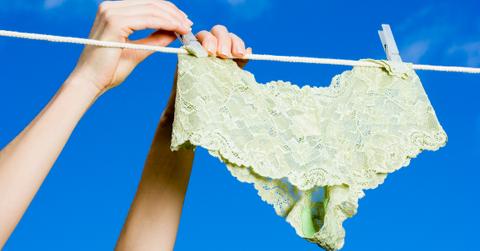 A pair of hands places lace green underwear on a clothing line outside