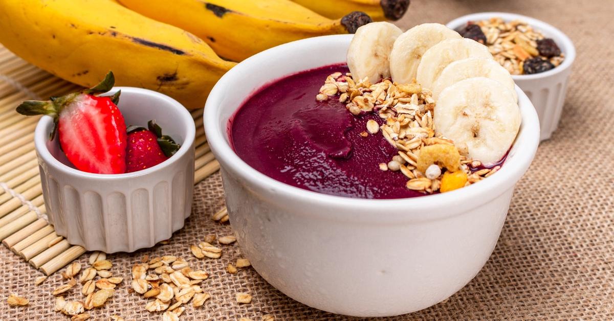 Açai bowl with bananas in a white bowl on a table with other fruit.