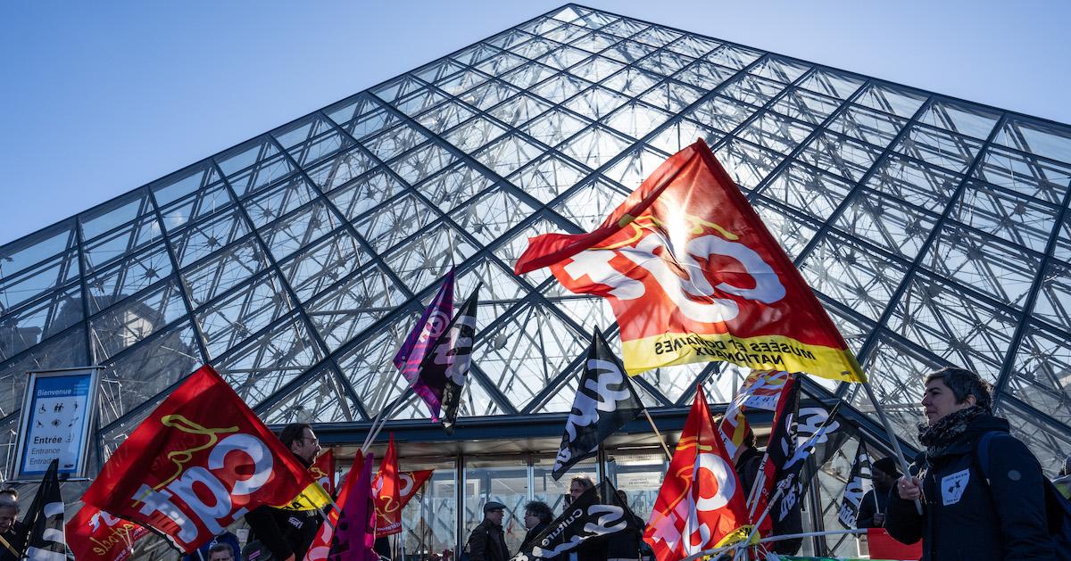 Striking union members wave flags in front of the Louvre Pyrmid.