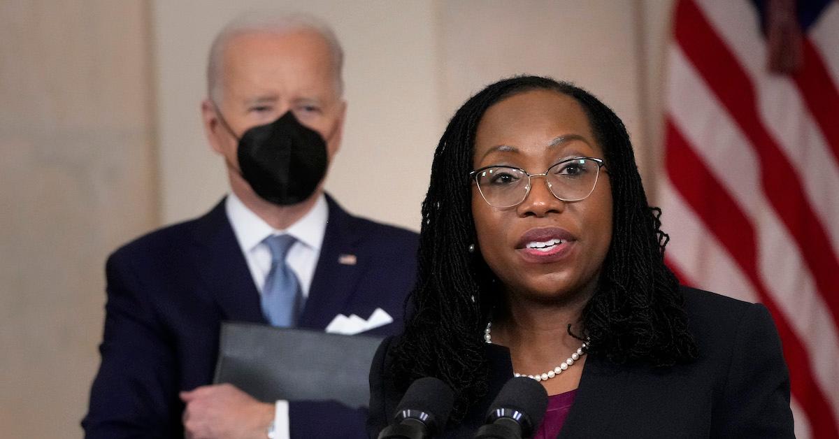 Ketanji Brown Jackson speaks at a press conference, with President Biden and an American Flag behind her.