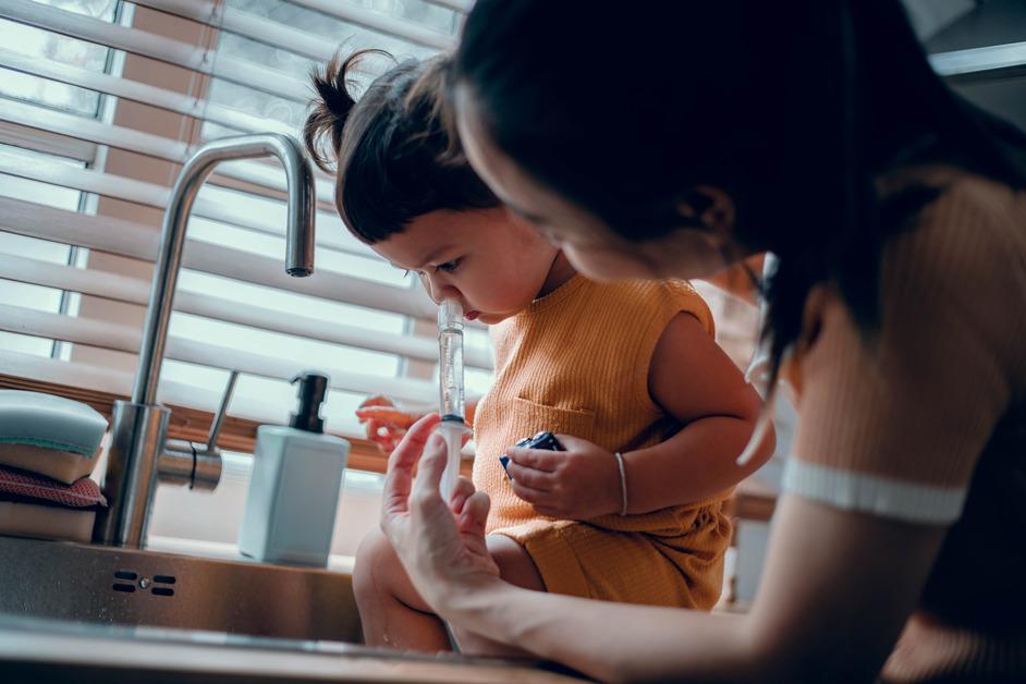 A woman uses a nasal syringe on her daughter's nose at the sink.