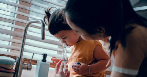 A woman uses a nasal syringe on her daughter's nose at the sink.