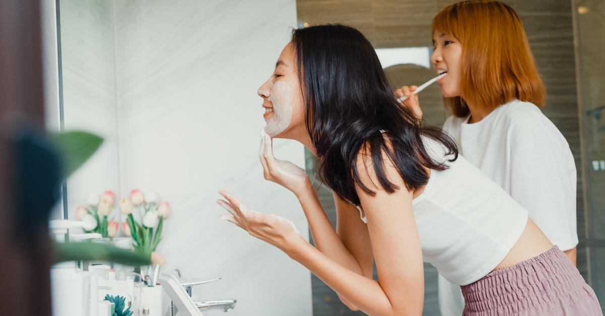 Two teens doing skincare in front of a mirror.