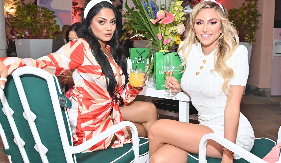 Two women wearing Mario Badescu skincare products sitting at a table and holding alcoholic beverages 