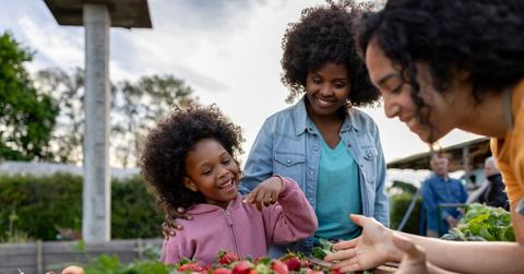 A smiling young girl and her mom purchase strawberries from a smiling farmers market vendor.