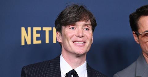 Cillian Murphy smiles at the camera on the red carpet with part of the Netflix logo behind him.