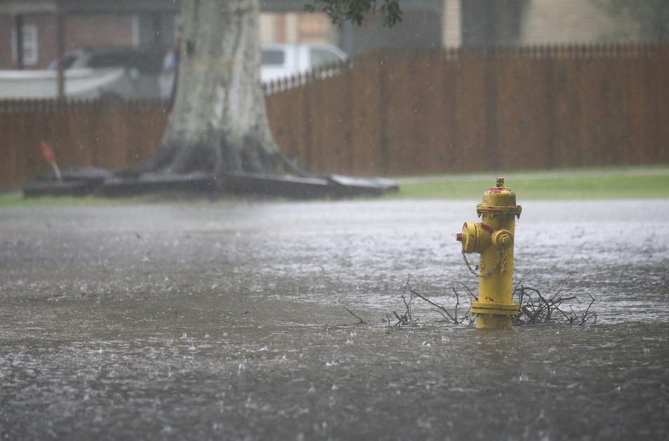 A stock photo of torrential rain hitting a yellow fire hydrant on a street during the day. 