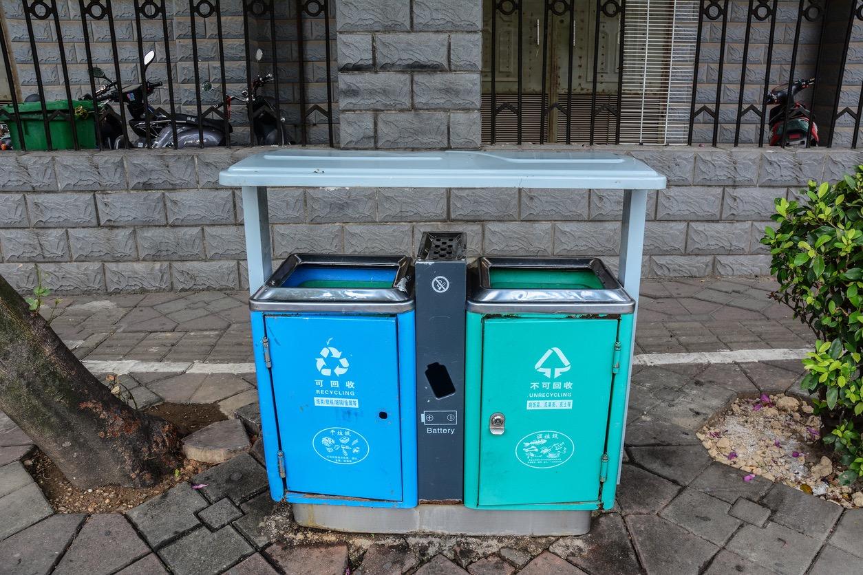 One blue and one teal recycling bin outside next to each other.