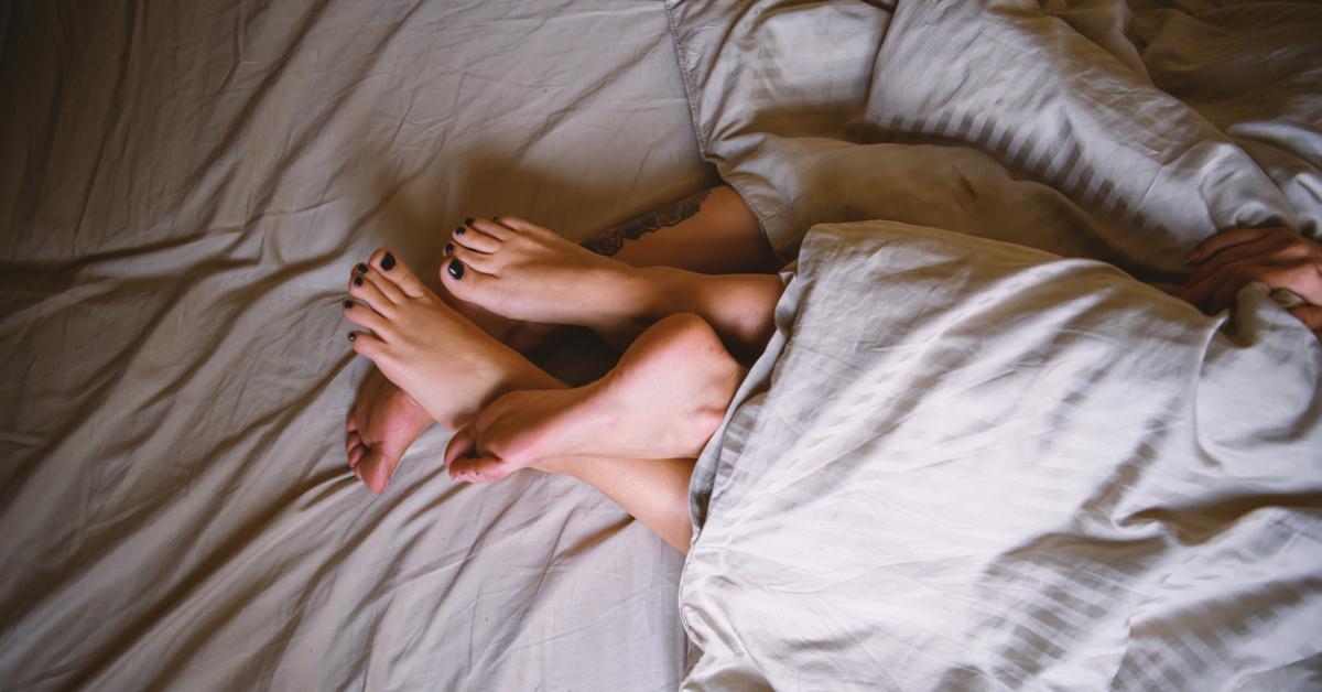 Photo of two pairs of feet intertwined in a bed