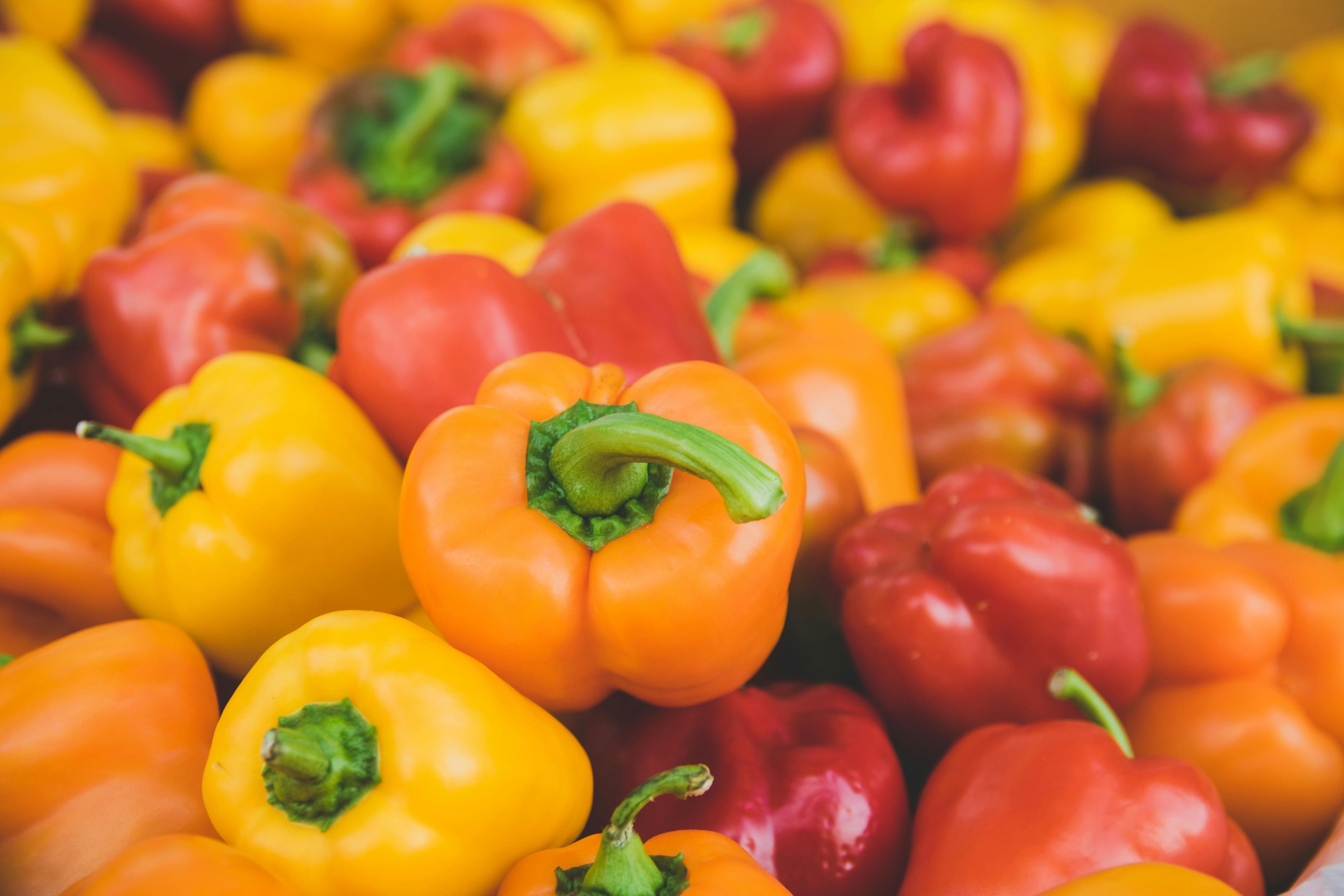 Orange, yellow, and red bell peppers are pictured stacked atop one another.