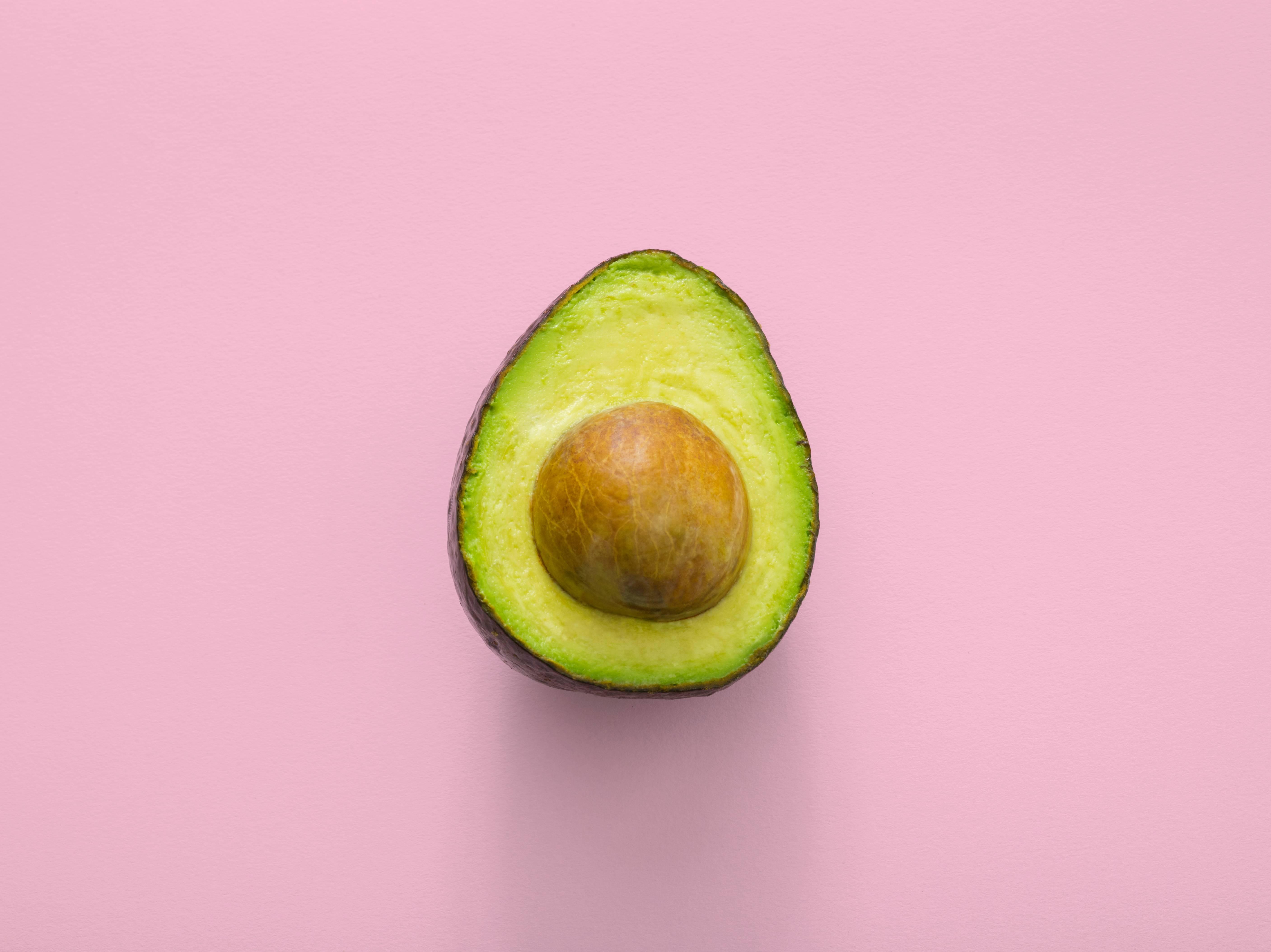 A sliced avocado is pictured in front of a pink background.