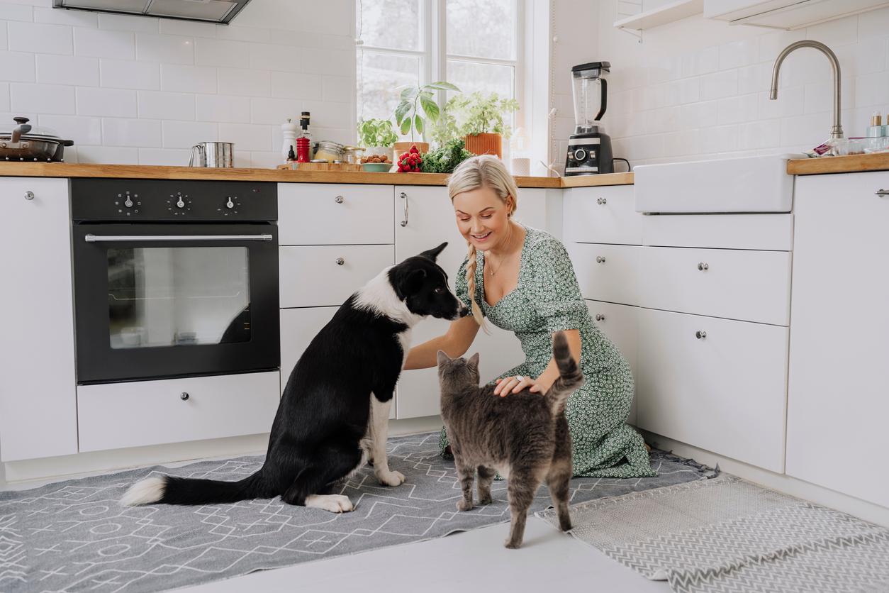 A pet parent smiles while bending down in her kitchen to pet her cat and dog.