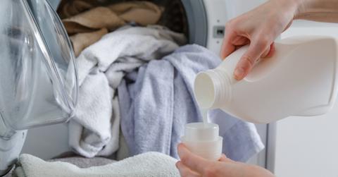 A person pours laundry soap into a cup in their laundry room.