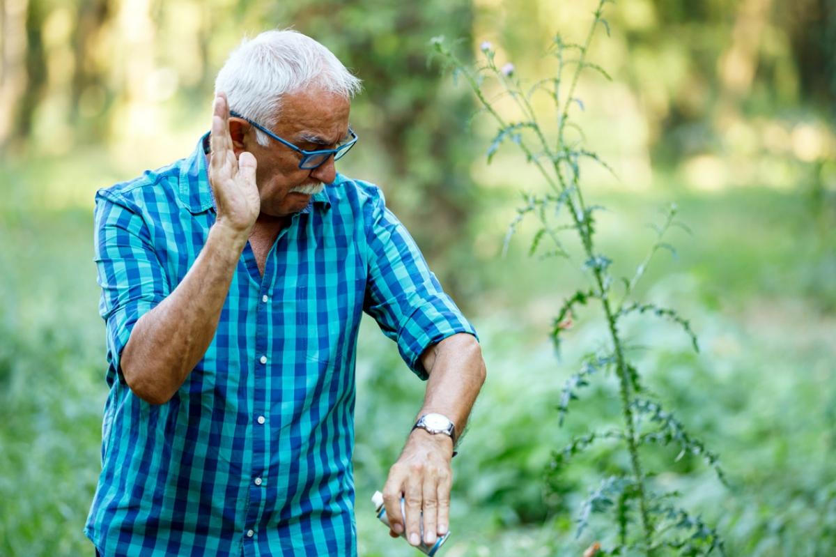 older male in checked shirt about to slap a mosquito