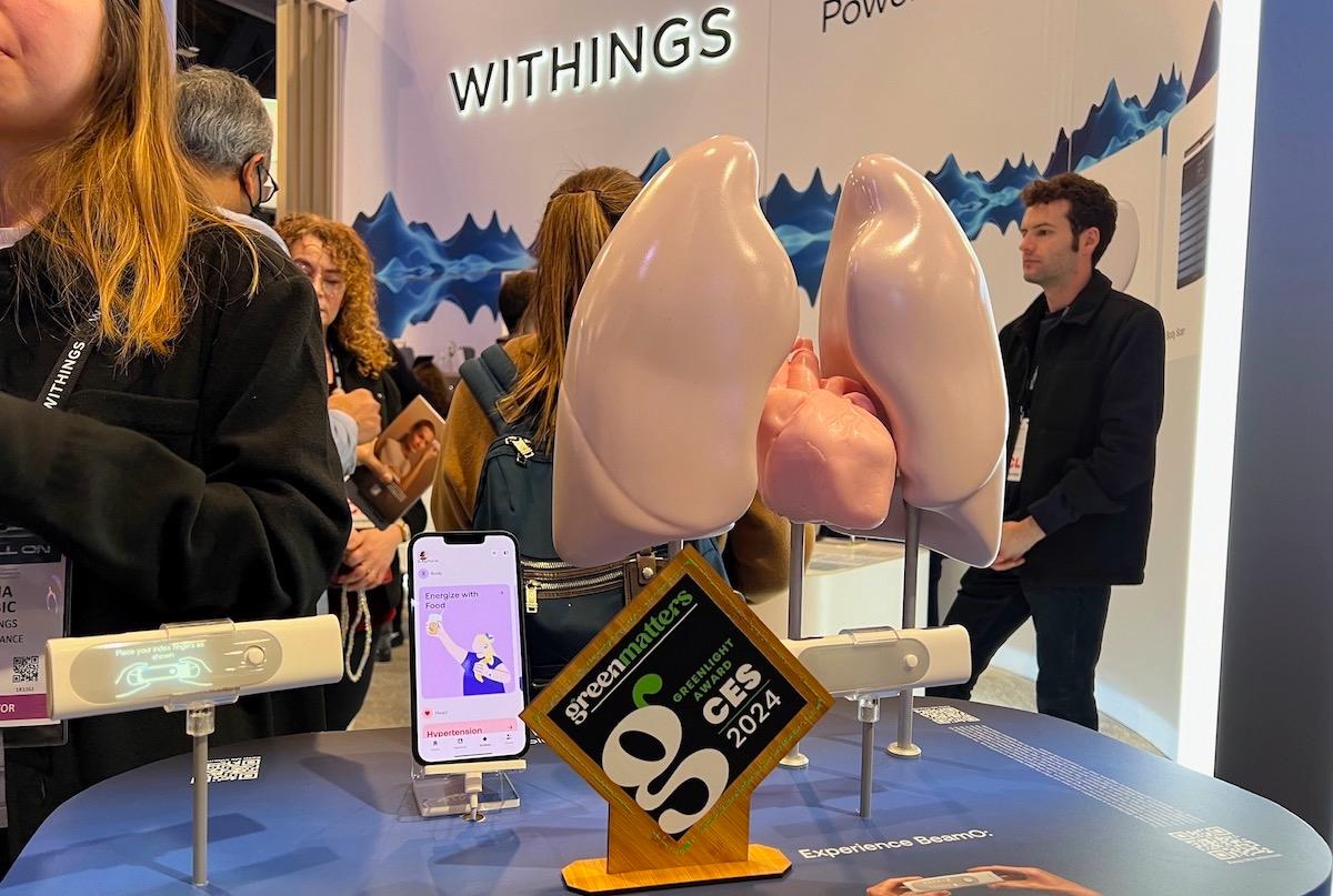 Withings' booth at CES, featuring a small white BeamO device, a wooden Green Matters Greenlight Award, an iPhone, and a plastic lung model.