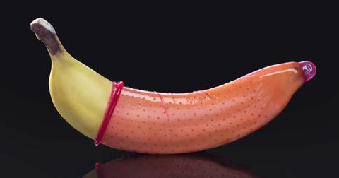 Photo of a pink condom on a banana in front of a black background
