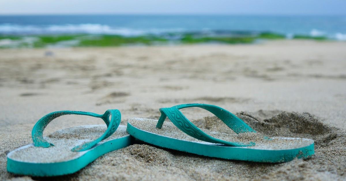 A pair of teal flip-flops sit on the sandy shore of a beach