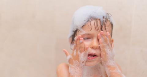 A little boy takes a bath and rubs soap out of his eyes.