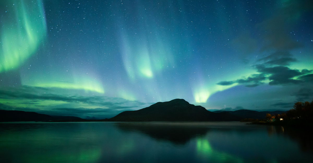 The northern lights shine above a lake and mountain