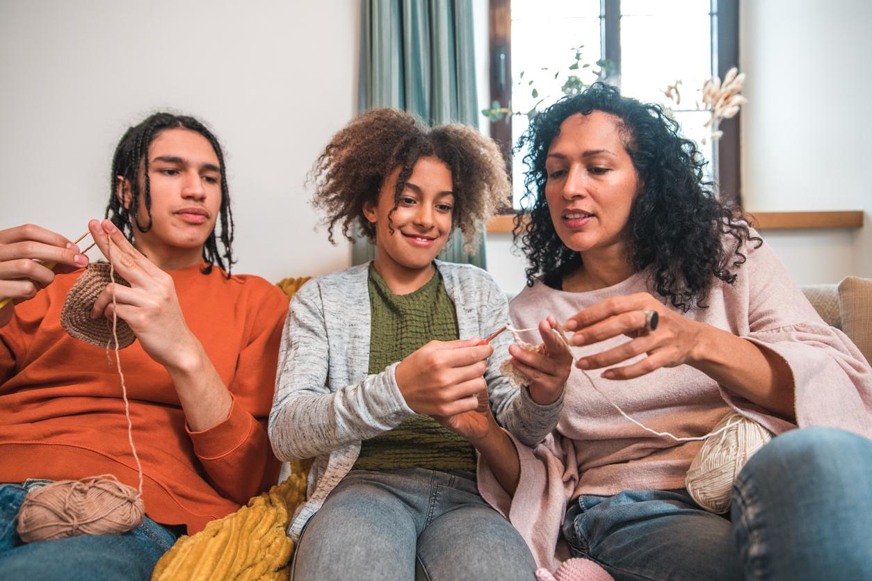 Three people of various ages sitting on a couch and working on crochet projects together.