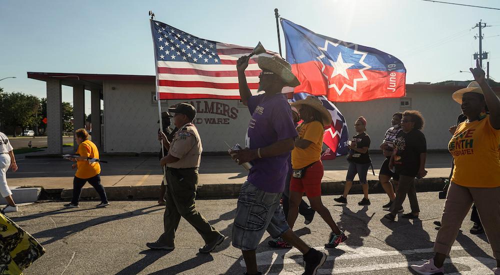 Protesters march on a street, carrying an American flag and a Juneteenth flag.