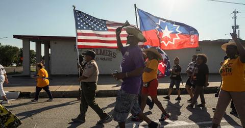 Protesters march on a street, carrying an American flag and a Juneteenth flag.