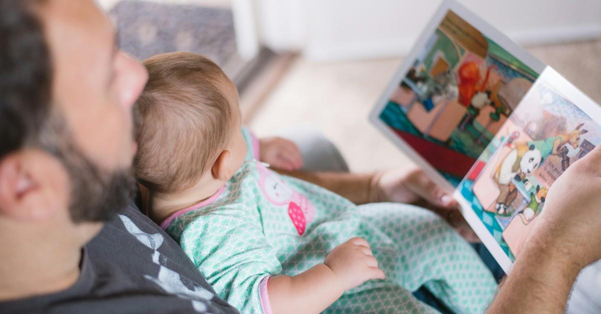 A dad holds a baby on his chest while reading a book