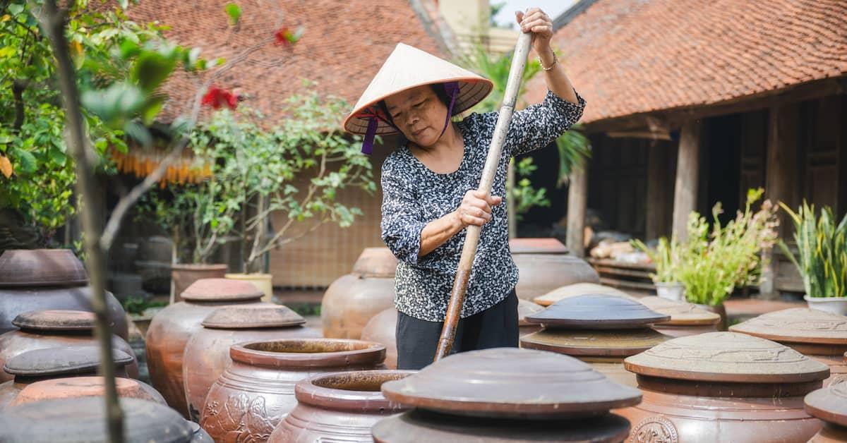 Person in a traditional soy fermentation plant stirring soy sauce in an ancient fermentation pot.
