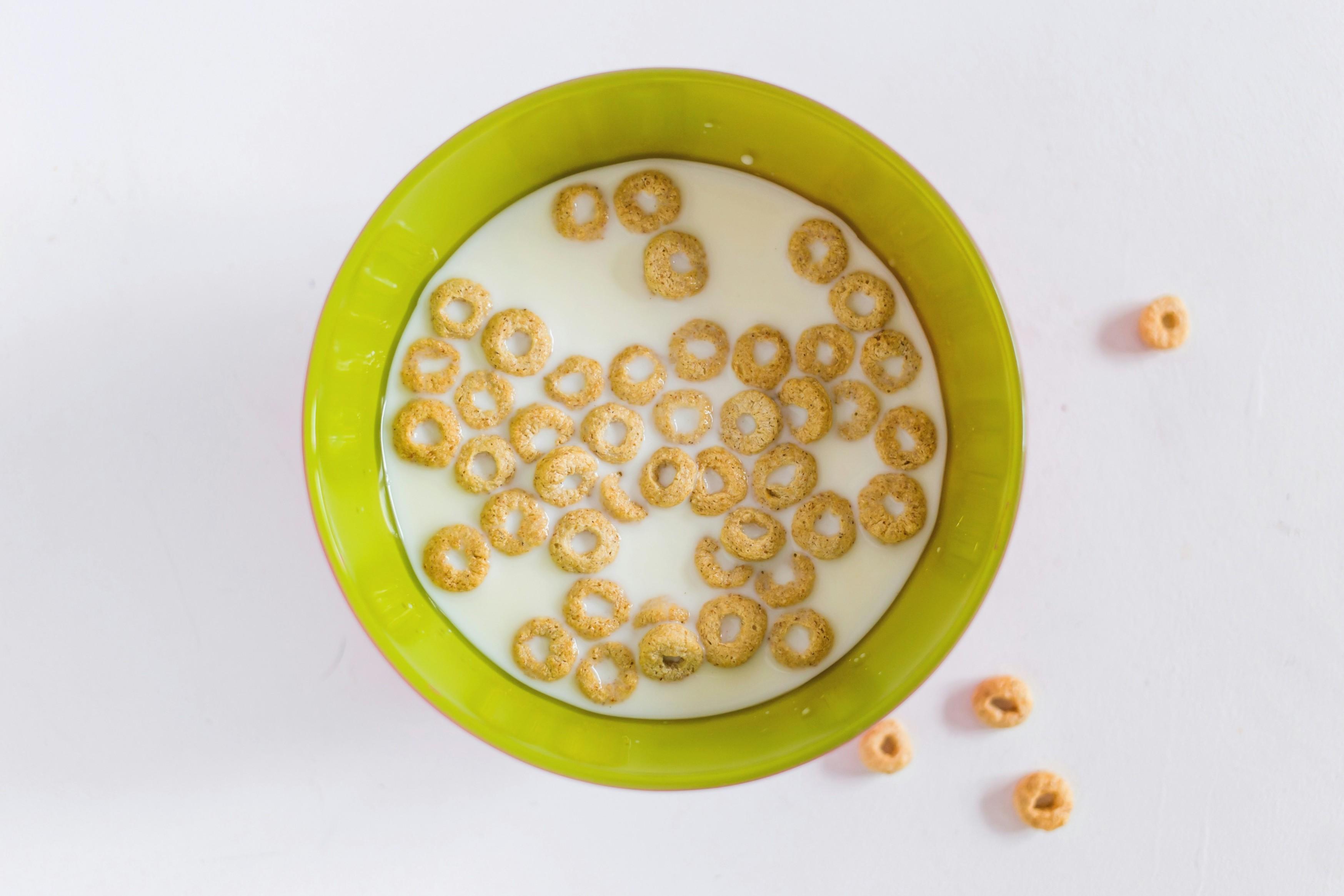 Cheerios are pictured floating in a green bowl of milk.