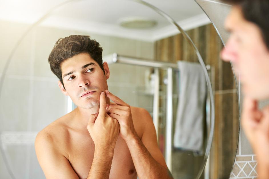 Man popping pimple while looking in bathroom mirror. 