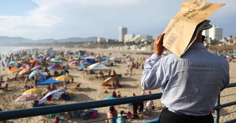 A person uses a piece of cardboard as a sunshade on Santa Monica Pier amid an intense heat wave in Southern California. (Cover Image Source: Getty Images | Mario Tama)