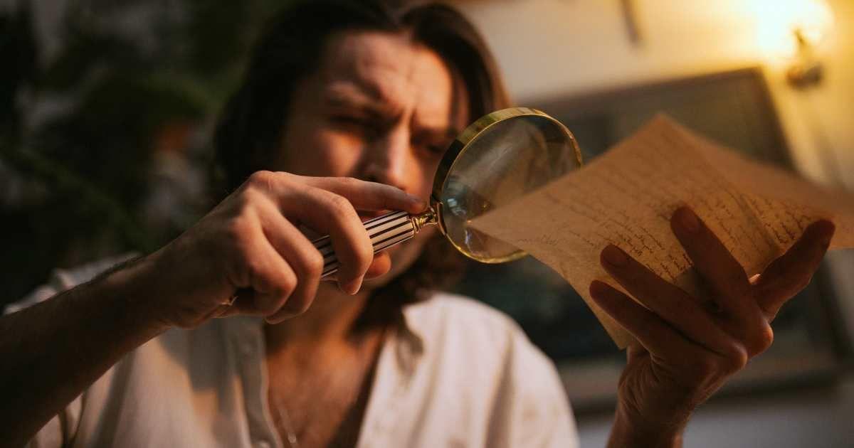 A man using a magnifying glass to read a vintage letter. (Representative Cover Image Source: PExels | KoolShooters)