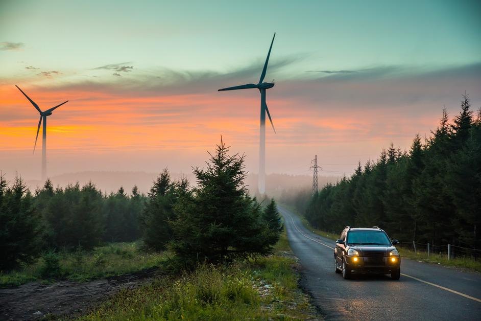 A car driving on a road with two wind turbines in the background.