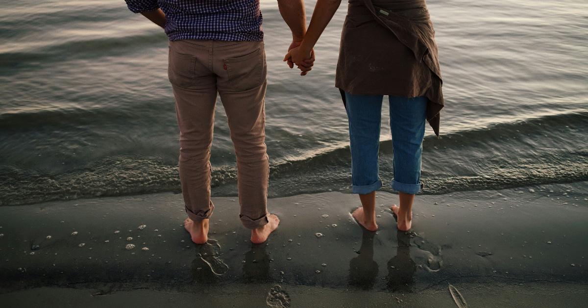 Two people barefoot on the beach walking into the waves. 