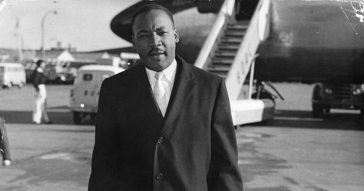 Martin Luther King Jr. in a suit on an airport tarmac, in a black-and-white image.