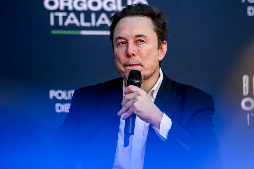 Elon Musk speaks into a microphone against a dark blue backdrop at the Atreju political convention organized by Fratelli d'Italia (Brothers of Italy) in December 2023 in Rome, Italy.