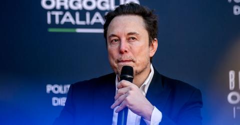 Elon Musk speaks into a microphone against a dark blue backdrop at the Atreju political convention organized by Fratelli d'Italia (Brothers of Italy) in December 2023 in Rome, Italy.