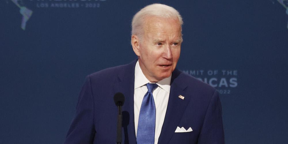 President Joe Biden makes a speech in front of a blue backdrop