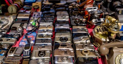 A large variety of vintage digital cameras and phones from the early 2000s spread out on a table.