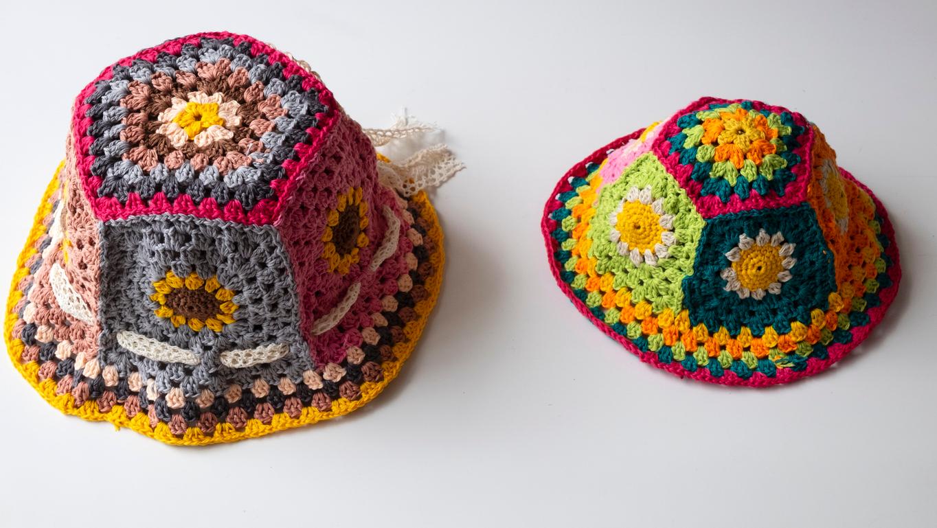 Two different sized crochet bucket hats made out of colorful granny squares with flowers side by side.